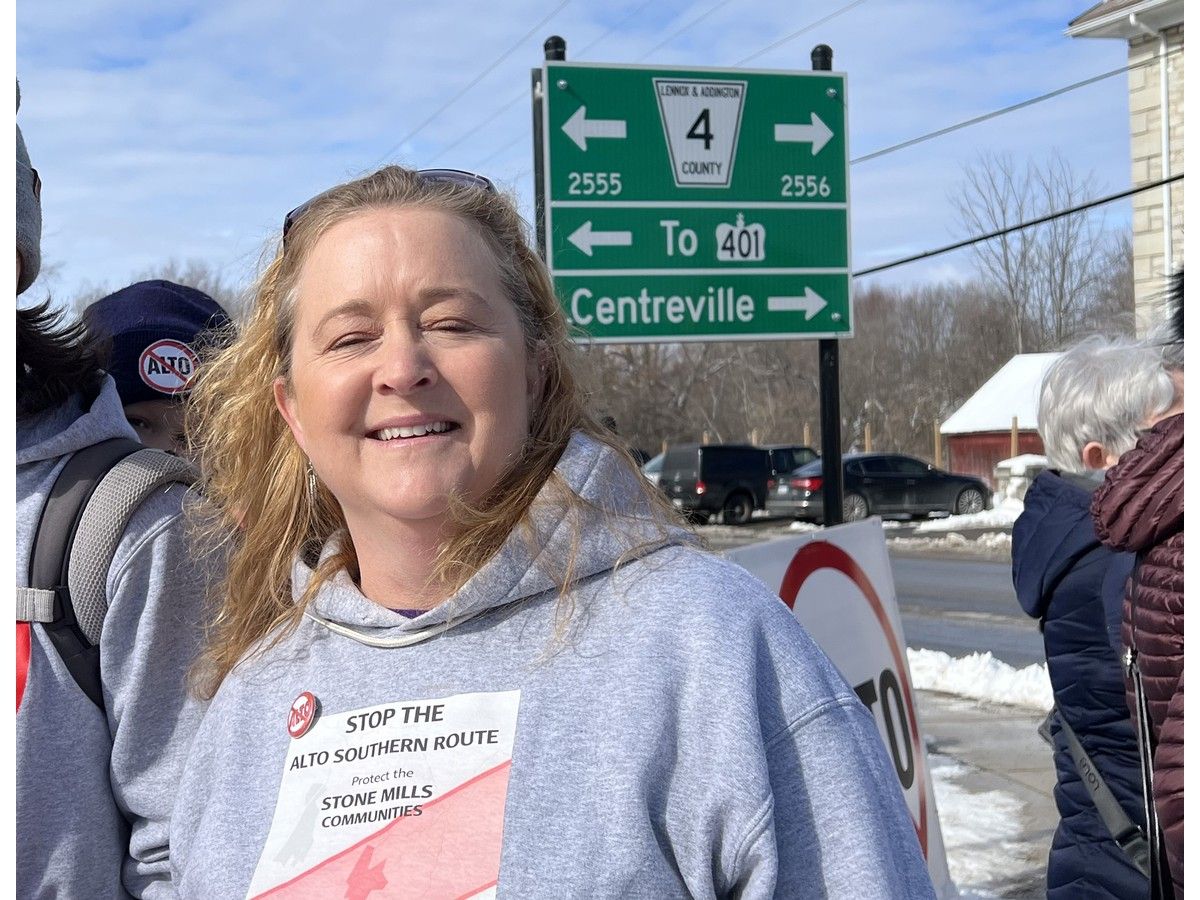 Stone Mills resident wearing a Stop the ALTO Southern Route hoodie beside a Lennox and Addington County road sign.